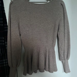 Beige ribbad topp med volang från ONLY Studio - Säljer en beige ribbad topp från ONLY Studio med långa ärmar och volang nertill. Tröjan har en figurnära passform och är tillverkad i mjukt material som passar perfekt till både jeans och kjol.