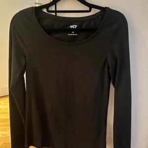 Svart långärmad topp från 157 - En enkel och stilren svart långärmad topp från 157 i mjuk bomullsblandning med stretch. Rundad halsringning och figurnära passform, perfekt att matcha med jeans eller kjol. Säker även denna i pris då den är ny utan prislapp 
