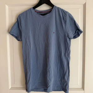 Blå t-shirt från Tommy Hilfiger - Snygg ljusblå t-shirt från Tommy Hilfiger i slim fit-modell. Tillverkad i ekologisk bomull och har en liten broderad logga på bröstet. Klassisk rund halsringning och korta ärmar. Perfekt för en stilren och enkel look.