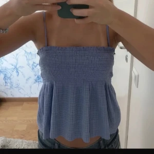 Ljusblå croppad linnetopp - Säljer en ljusblå croppad linnetopp med smala axelband och rynkad överdel. Toppen har en luftig och vågig nederkant, perfekt för varma dagar. Enkel och stilren design som passar till jeans eller kjol.