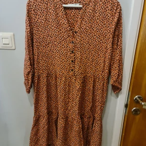 Mönstrad klänning från b.young - Säljer en brunmönstrad klänning från b.young i storlek M (EUR 38). Klänningen har v-ringning, knappar framtill och trekvartsärm. Den har ett prickigt mönster i svart och vitt samt volangdetaljer nedtill. Perfekt för dig som gillar en avslappnad men trendig stil.
