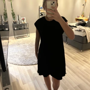 Svart kortärmad klänning - Enkel svart klänning med korta ärmar och rak passform. Klänningen är knälång och har en minimalistisk design utan synliga detaljer eller mönster. Perfekt för dig som gillar stilrena plagg.