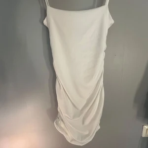 Vit kort klänning med drapering - Säljer en stilren vit klänning med smala axelband och snygg drapering längs sidan. Klänningen är figurnära med en elegant, enkel design. Perfekt för dig som gillar minimalistisk stil. Helt oanvänd!💓