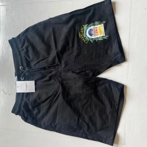Svarta shorts från Casablanca med tryck - Svarta shorts från Casablanca med färgglatt tryck framtill och elastisk midja med snörning. Tillverkade i mjuk bomull, perfekt för avslappnade dagar. Snygg och enkel design med en unik detalj på benet.