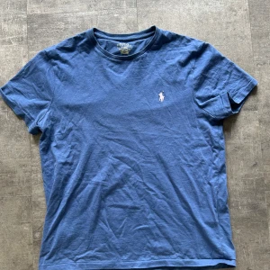 Blå t-shirt från Polo Ralph Lauren - Säljer en blå t-shirt från Polo Ralph Lauren med klassisk rund halsringning och broderad logga på bröstet. Modellen är slim fit och tillverkad i mjuk bomull. Perfekt för en stilren och avslappnad look. 