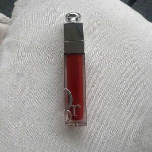 Dior Addict Lip Maximizer 028 - Säljer ett Dior Addict Lip Maximizer läppglans i färgen 028. Glanset har en intensiv röd nyans och kommer i en lyxig genomskinlig hylsa med silverdetaljer och Dior-logga. Perfekt för att ge läpparna extra glans och volym. Kommer utan förpackning, oanvänd och otestad, om du köper fler av dessa läppstift kan jag tänka mig bättre pris. Rensning inför flytt