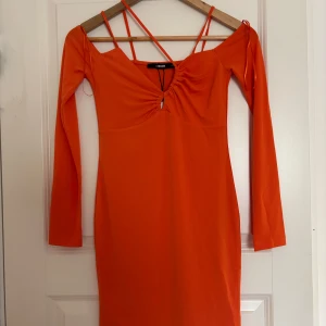 Orange långärmad klänning från Bik Bok - Trendig orange klänning från Bik Bok med långa ärmar och smala axelband. Klänningen har en snygg rynkdetalj framtill vid bysten och en figurnära passform. Perfekt för dig som vill sticka ut med färg. Nypris 399kr