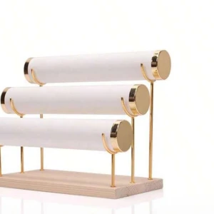 Smyckesställ i vitt och guld - Stilrent smyckesställ med tre cylindriska stänger i vitt och detaljer i guld. Stället har en bas i ljust trä och passar perfekt för att organisera armband, klockor eller halsband. Snygg och modern design som lyfter din smyckesförvaring.