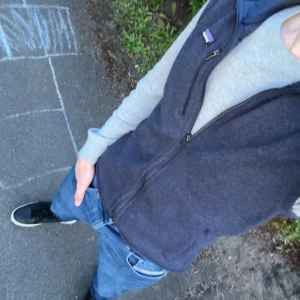 Mörkblå fleeceväst från Patagonia - Säljer en mörkblå fleeceväst från Patagonia med dragkedja framtill och två fickor med dragkedja. Västen har en hög krage och klassisk passform, perfekt för lager-på-lager-stil.