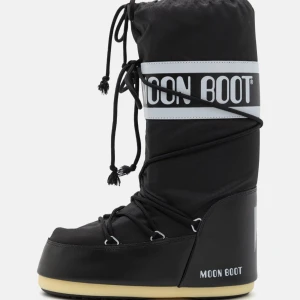 Svarta Moon Boots med snörning - Säljer ett par klassiska svarta Moon Boots med vit logga och snörning upptill. Skorna har en hög och vadderad design med platt sula och är perfekta för kalla vinterdagar. Ikonisk look och superbekväma att ha på sig.