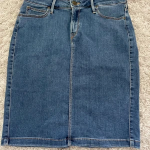 Jeanskjol från Lee - Klassisk blå jeanskjol från Lee med normal passform. Kjolen har fickor både fram och bak, bälteshällor och en liten slits bak. Storlek 38