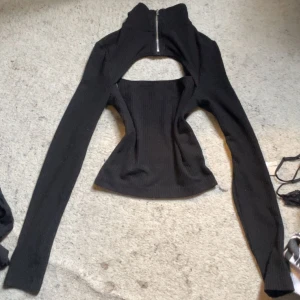 Svart croppad bolerotopp med dragkedja - Trendig svart croppad bolerotopp med lång ärm och hög krage. Toppen har en synlig dragkedja framtill och är tillverkad i ett ribbat material som ger en snygg passform.