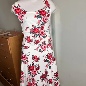 Vit blommig klänning  - Säljer en vit långklänning med vackert blommigt mönster i rosa och röda toner. Klänningen är ärmlös med rundad halsringning och har en mjuk, följsam passform. Perfekt för sommarens alla tillfällen!