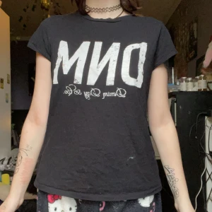 Svart t-shirt med vit text från Denim - Svart t-shirt med stor vit text 'DNM' och mindre text under på bröstet. Klassisk rund halsringning och korta ärmar. Perfekt för en avslappnad och cool stil.