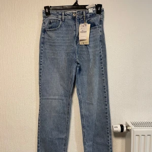 Blå raka jeans från STR Teen - Säljer ett par klassiska blå jeans från STR Teen med rak passform och hög midja. Jeansen har fem fickor och stängs med dragkedja och knapp. Perfekta till vardags och enkla att matcha med olika toppar. Helt nya med prislappen.