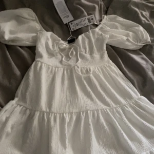 Vit puffärm klänning från Gina tricot - Supersöt vit klänning med puffärmar och knytning framtill från Gina tricot. Klänningen har en lätt rynkad struktur och en luftig, flowy passform. Perfekt för sommarens alla tillfällen. Mini-längd och rundad halsringning. Har aldrig bärt den! Helt ny med prislapp också!🌸🌸