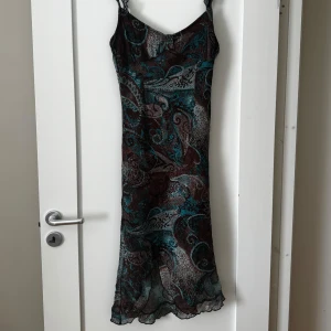 Mönstrad långklänning med tunna axelband - Säljer en långklänning med tunna axelband och vackert mönster i brunt, turkost och vitt. Klänningen har en lätt, luftig känsla och är perfekt för varma dagar. Materialet är tunt och faller snyggt. Passar dig som gillar bohemisk stil.