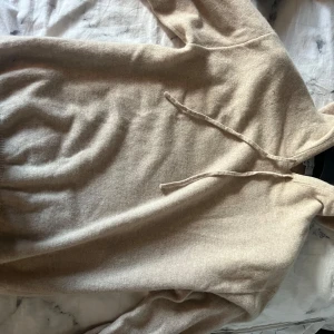 Beige 100% kashmir hoodie  - Säljer en beige 100% kashmir hoodie i mjukt material. Tröjan har huva med dragsko och långa ärmar. Perfekt för en avslappnad stil och enkel att matcha med andra plagg.