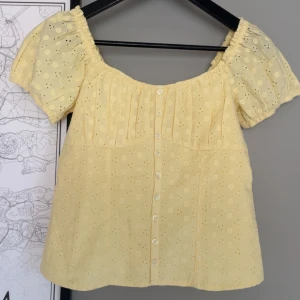 hollister topp - Söt ljusgul blus med korta puffärmar och broderade blommor. Blusen har knappar framtill, resår vid axlarna och smock i ryggen för en bekväm passform. Perfekt för vår och sommar! köpt helt ny, prislapp kvar helt slut på hemsidan 