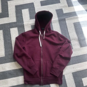 Vinröd zip up från Polo Ralph Lauren - Säljer en vinröd hoodie från Polo Ralph Lauren med dragkedja och vit snörning i huvan. Klassisk broderad logga på bröstet. Perfekt för en avslappnad stil. Passar bra på dig som är cirka 170-180cm! Hör av er om ni har frågor✌️