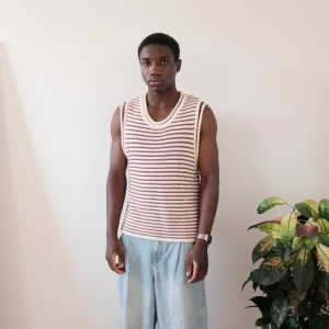 Randig stickad väst från Zara - Säljer en ärmlös stickad väst från Zara med bruna och vita ränder. Västen har rund halsringning och är i en mjuk, bekväm stickad kvalitet. Perfekt att styla över en t-shirt eller skjorta.  Size S  Bröst:47cm Längd:60cm