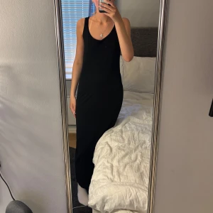 Svart långklänning med v-ringning - En stilren svart långklänning med v-ringad hals och smala axelband. Klänningen har en figurnära passform och är perfekt för dig som gillar enkel och tidlös stil. Passar till många olika tillfällen och är lätt att matcha med accessoarer.