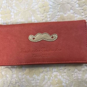Färgglad plånbok med mustaschdetalj - Säljer en unik plånbok i syntetmaterial med en söt beige mustaschdetalj på framsidan. Insidan har flera fack i rosa, blått och gult samt ett myntfack med dragkedja. Perfekt för dig som gillar färg och lekfull design!