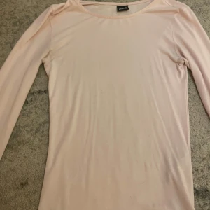 Ljusrosa långärmad topp från Gina! - En enkel och stilren ljusrosa långärmad topp från Gina. Modellen är figurnära med rund halsringning och mjukt, stretchigt material som passar perfekt till många olika outfits.