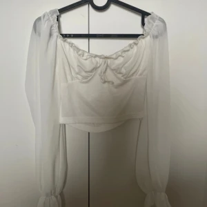Vit offshoulder topp med långa ärmar - Säljer en vit offshoulder topp med långa, transparenta ärmar och knytning framtill. Toppen är croppad och är i fint skick