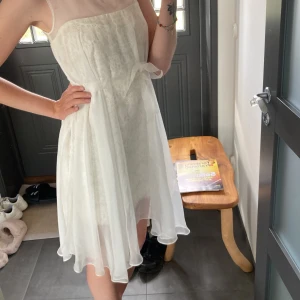 Vit spetsklänning från Ida Sjöstedt - Superfin vit klänning från Ida Sjöstedt med spetsdetaljer och transparent mesh upptill. Klänningen har ett tunt band i midjan som knyts till rosett och ett luftigt, svävande tyg. Perfekt för sommarens tillfällen!