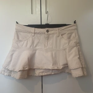 Beige volangkjol i jeansmaterial - Säljer en beige/vit kortkjol i jeansmaterial med volangdetalj nedtill. Volangerna går såklart att stryka ut bara jag som varit lat!