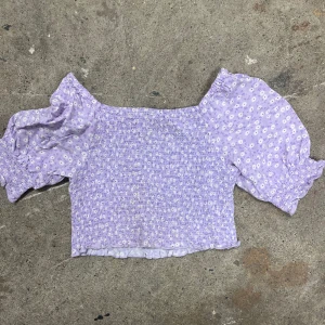 Ljuslila blommig topp med puffärmar - Supersöt ljuslila topp från Kappahl med små vita blommor och smockad kropp. Toppen har korta puffärmar och volangkant nedtill. Perfekt för en somrig look!