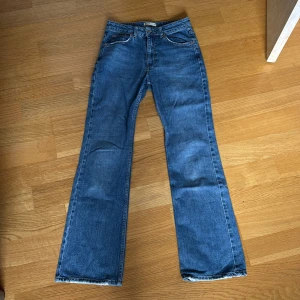 Blå bootcut jeans från Gina Tricot - Säljer ett par klassiska blå bootcut jeans med medelhög midja från Gina Tricot. Har lite slitningar längst ner på benen. Jeansen har normal passform, fem fickor och är tillverkade i ett tåligt denimtyg. Perfekta för dig som gillar en tidlös stil med lite vidare ben.