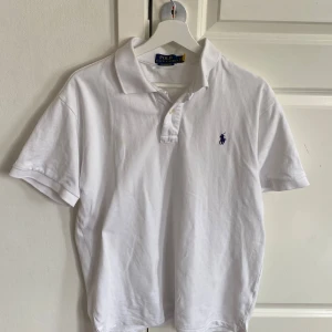 Vit piké från Polo Ralph Lauren - Klassisk vit pikétröja från Polo Ralph Lauren med blå broderad logga på bröstet. Tröjan har korta ärmar, krage och knappar vid halsen. Modellen är custom slim fit och bara använd ett fåtal gånger och är i strl L, hör av er om ni vill ha fler bilder och de finns även en qr kod i den som leder till polo ralph luraen hemsidan