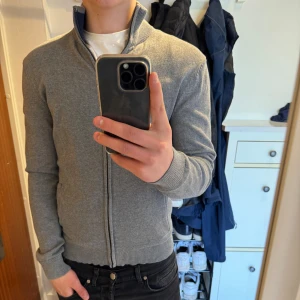Grå ziptröja - Säljer en stilren grå ziptröja med hög krage och ribbade muddar. Tröjan har dragkedja hela vägen och är tillverkad i ett mjukt material som passar perfekt till vardags. Enkel och klassisk design utan synliga loggor. Passar till det mesta. Priset är ej hugget i sten💰hör av dig vid minsta fråga eller fundering!!