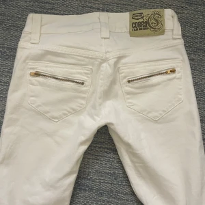 Vita jeans med dragkedjedetaljer  - Säljer ett par vita jeansbyxor från Cipo & Baxx med snygga dragkedjor på fickorna både fram och bak. Byxorna har raka ben, normal passform och klassisk knappstängning. Perfekta för dig som vill sticka ut med detaljer. Stl W24 L32, skulle säga en XS