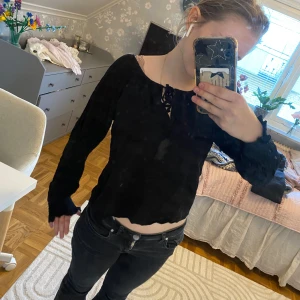 Svart croppad blus med knyt - Säljer en svart croppad blus med långa ärmar och knytning vid halsen. Ärmarna har smockade muddar och blusen har en lätt volangkant nertill. Perfekt för en trendig och stilren look.