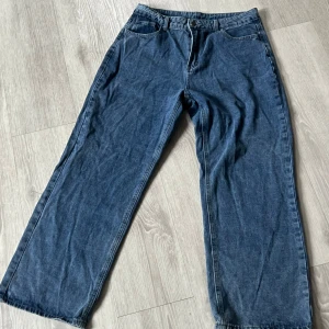 Blå wide jeans - Säljer ett par blåa jeans med breda ben och klassisk femficksdesign. Jeansen har normal passform och stängs med dragkedja och knapp. Perfekta för en avslappnad och trendig stil.