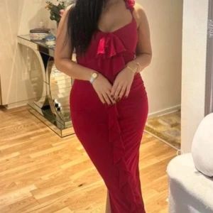 Röd långklänning med volangdetaljer - Säljer en snygg röd långklänning med volang framtill och smala axelband i storlek S. Klänningen har en tight passform och en liten slits nertill. Perfekt för dig som vill sticka ut på festen!