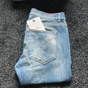 Dondup jeans ( sommarens hit ) - - betala nypris få joluca, Säljer ett par ljusblå jeans från Dondup med slitna detaljer och klassisk femficksdesign. Jeansen har raka ben och normal passform, samt gylf med dragkedja och knapp. Perfekta för en avslappnad stil.