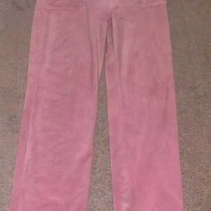 Rosa juicy byxor - Säljer ett par rosa byxor i mjuk mocka med raka, vida ben och stora fickor bak med knappar. Byxorna har hög midja och en snygg, retroinspirerad look. Perfekta för dig som vill sticka ut med färg och material!