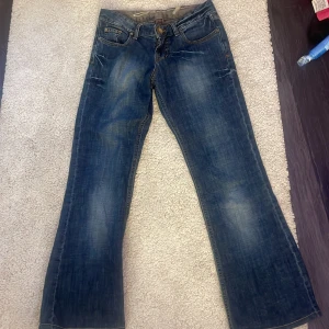 Blå jeansbyxor från Seven7 med strasstenar - Säljer ett par blå jeansbyxor från Seven7 med snygga strasstenar på bakfickorna. Byxorna har klassisk femficksdesign, normal passform och bootcut-stil. Perfekta för dig som vill ha ett par jeans med lite extra detaljer.