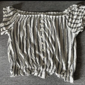 Vit och svart randig blus med knappar - Säljer en söt vit blus med svarta ränder och knappar framtill. Blusen har korta ärmar med volang och resår i nederkant för en fin passform. Perfekt till sommaren och enkel att matcha med jeans eller kjol.