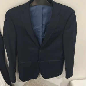 Kostym  - Säljer min mörkblåa kostym från dressman som jag har använt 1 gång. Säljer den då jag har vuxit ur den. Kavajen har storlek 42 short vilket betyder att den är kortare i ärmarna och byxorna 29-30. Kostymen passar någon runt 165-172. Nypris 2499kr