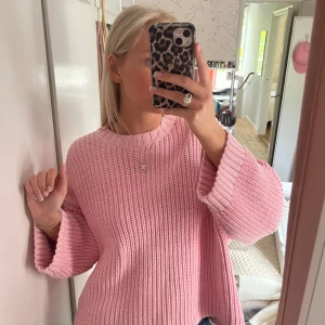 Rosa stickad tröja med breda ärmar - Säljer en söt rosa stickad tröja med breda, långa ärmar och rund halsringning. Tröjan har en avslappnad passform och är perfekt att styla med jeans eller kjol. Supermysig och trendig för kyligare dagar!