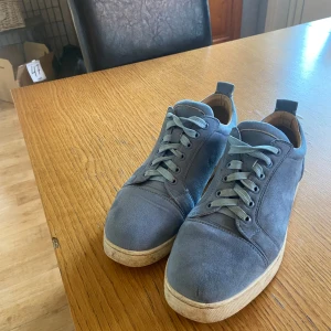 Loubitins - Snygga blå sneakers i mocka från Christian Louboutin med klassisk röd sula och vita kanter. Skorna har rund tå, platt sula och snörning framtill. Perfekta för dig som vill sticka ut med en exklusiv touch och cool färg på fötterna. Låda och påse kommer med.