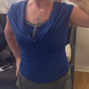 Kornblå topp med pärldetaljer Bodyflirt - Supersnygg kornblå topp från Bodyflirt med draperad halsringning och glittrande pärldetaljer längs urringningen. Toppen är ärmlös och har en tight passform som framhäver figuren. Perfekt för dig som vill sticka ut med lite extra bling.