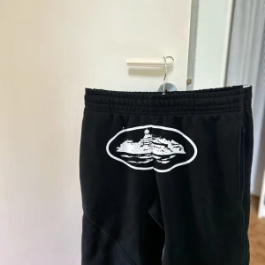 Svarta Corteiz shorts med tryck från Alcatraz  - Svarta shorts från märket Corteiz med elastisk midja.  På framsidan finns ett stort vitt tryck av Alcatraz fängelset. Shortsen är tillverkade av en blandning bomull och polyester. Shortsen har en avslappnad passform. Pris kan diskuteras!