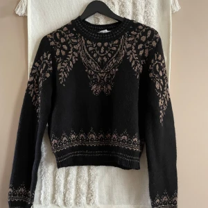 Svart stickad tröja med mönster från Zara - Svart stickad tröja från Zara med ljusbrunt mönster över bröst, ärmar och nederkant. Tröjan har rund halsringning, långa ärmar och en lite croppad passform. Perfekt för dig som gillar unika detaljer och snygg design.
