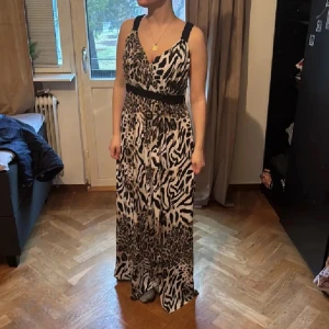 Långklänning med leopardmönster från Isolde - Snygg långklänning från Isolde med leopard- och zebramönster i svart, beige och vitt. Klänningen har breda flätade axelband, omlott-v-ringning och markerad midja. Perfekt för dig som vill sticka ut med ett djurmönstrat statement-plagg.